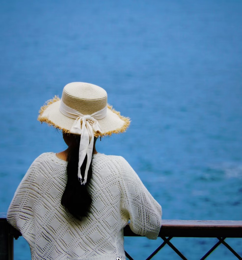 A woman in a straw hat looking out over the sea from a terrace
