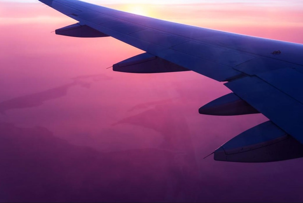 View from an aircraft window over land at sunset, wing in frame